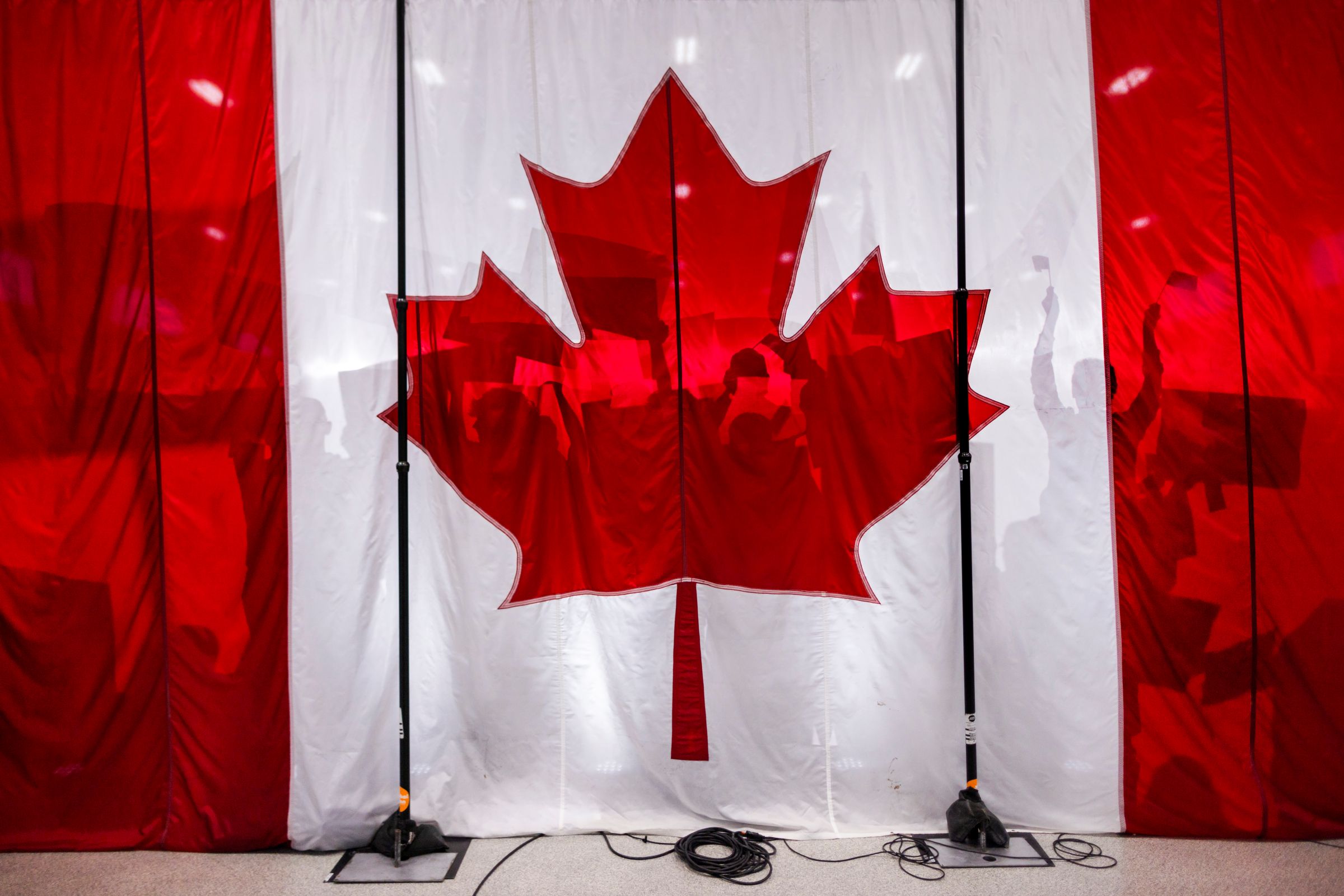 People in silhouette, some with arms up and holding signs, appear behind a Canadian flag.