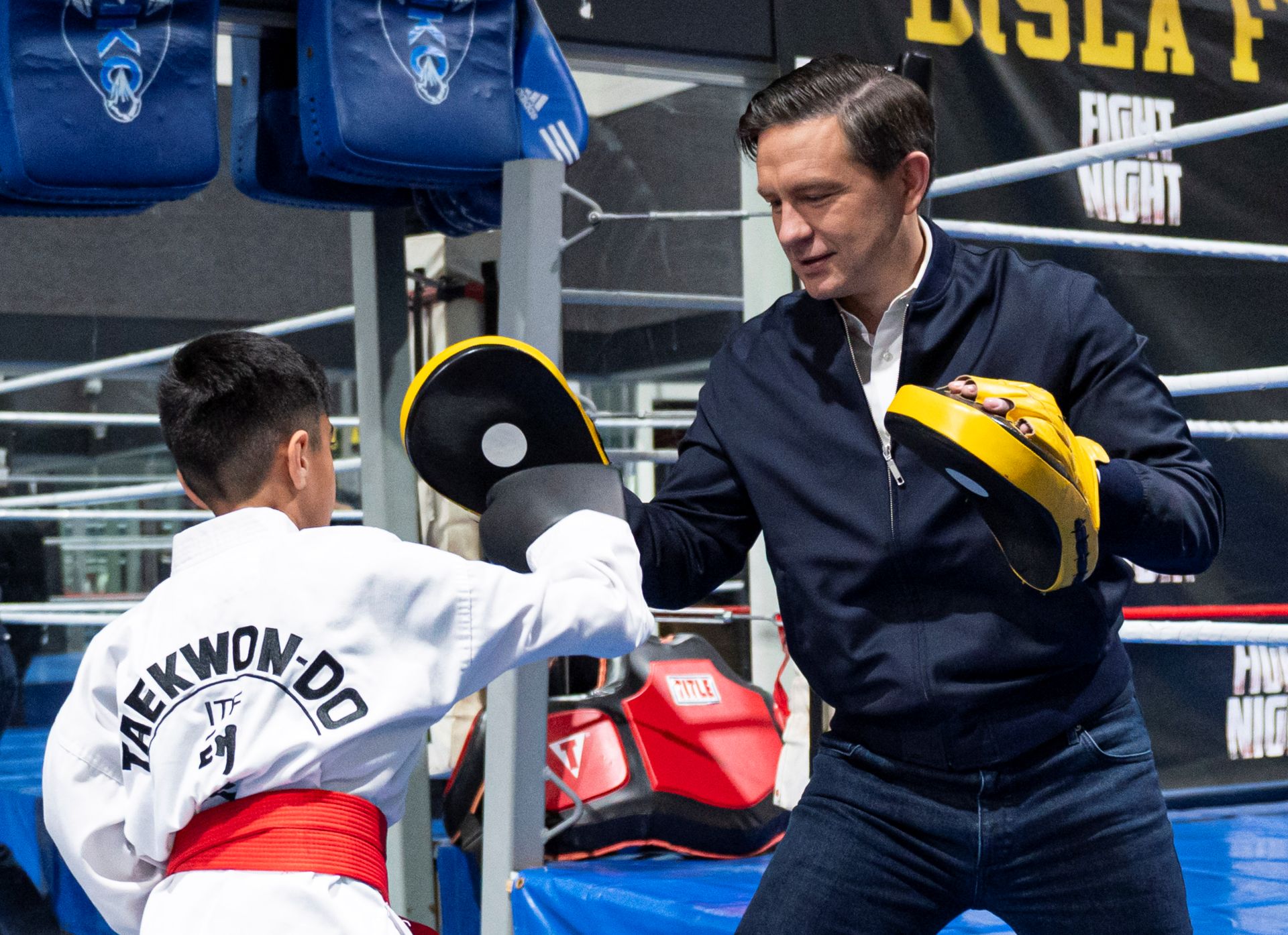 Pierre Poilievre sparring with a young Taekwon-do student with a boxing ring in the background.