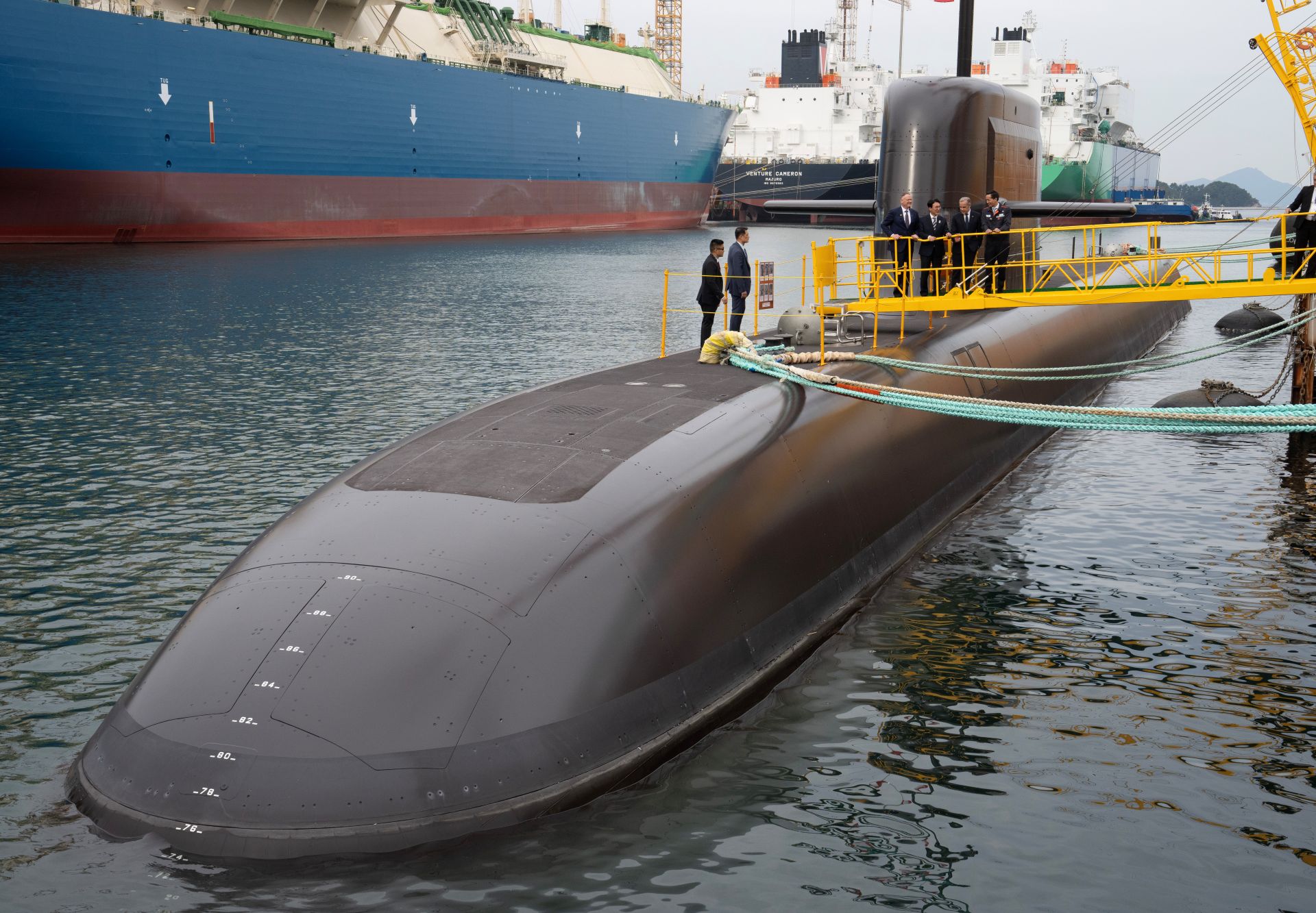 Four men in suits on a gangplank admiring a submarine.