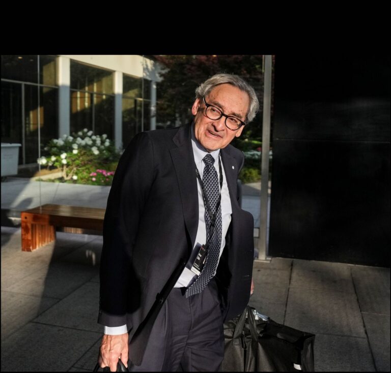 Michael Sabia walking outdoors, bags in each hand.