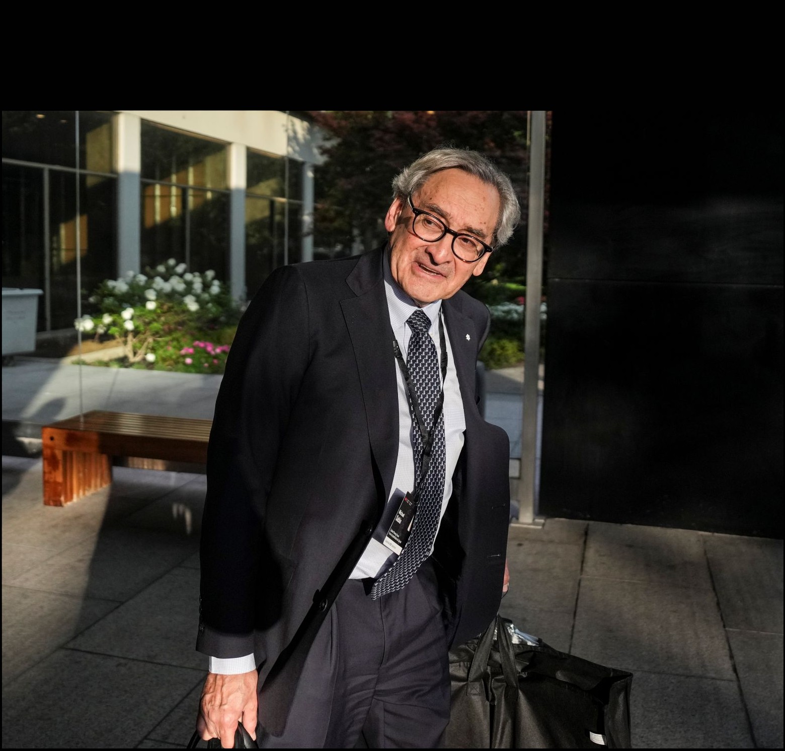 Michael Sabia walking outdoors, bags in each hand.