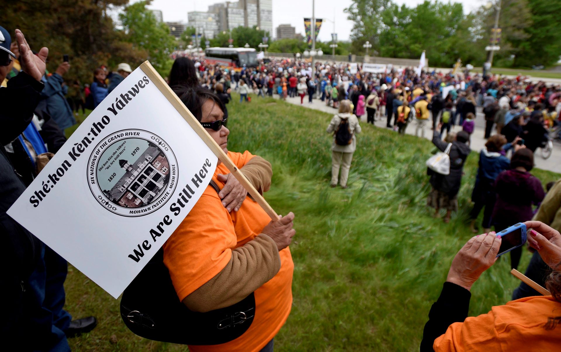 Une foule en procession avance sur une route bordée de supporteurs, quelques-uns vêtus de chandails orange.