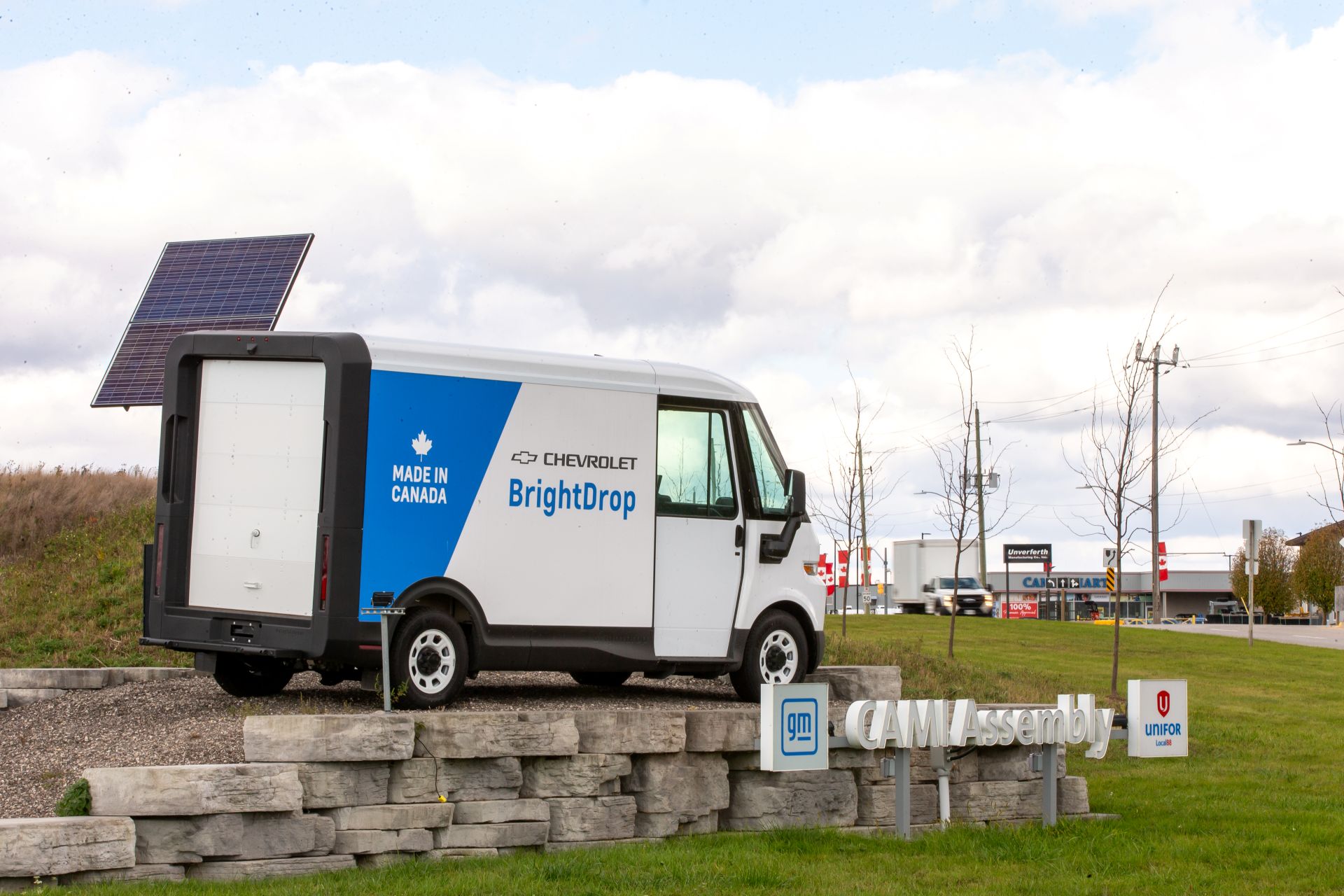 A white BrightDrop cube van at the entrance of a GM assembly plant with Made in Canada written on the side.