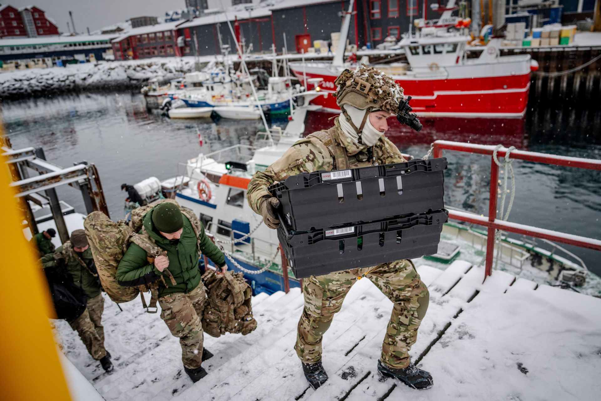 Four soldiers climbing snowy steps carrying gear from a boat.