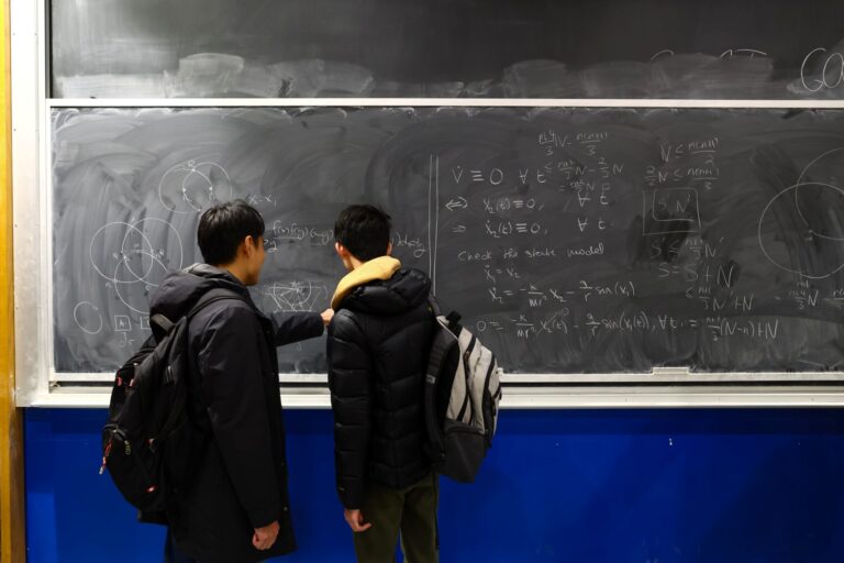 Two boys at a chalkboard covered in math problems.