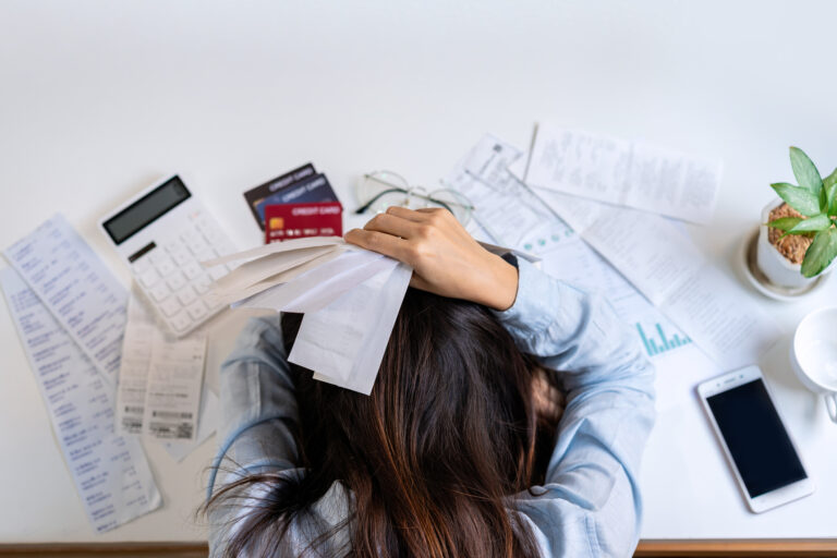 A woman dealing with a pile of bills with a calculator photographed from above.