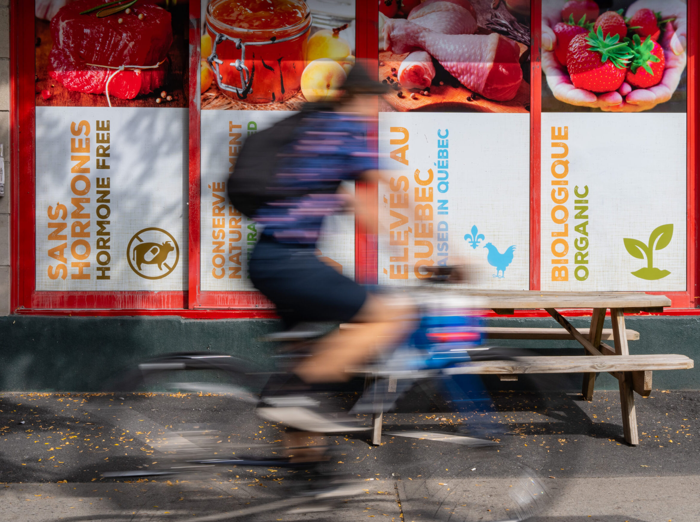 Un cycliste passe devant un commerce avec des affiches en anglais et en français, à Montréal
