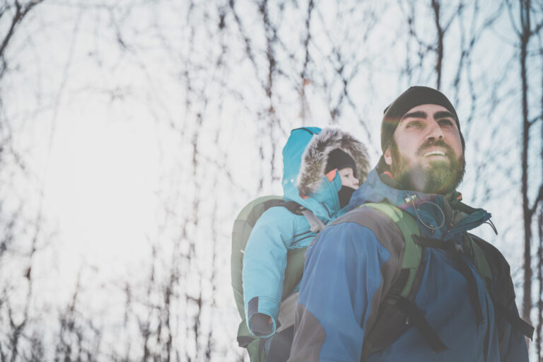 A young father hiking in a winter landscape with a baby in a carrier.