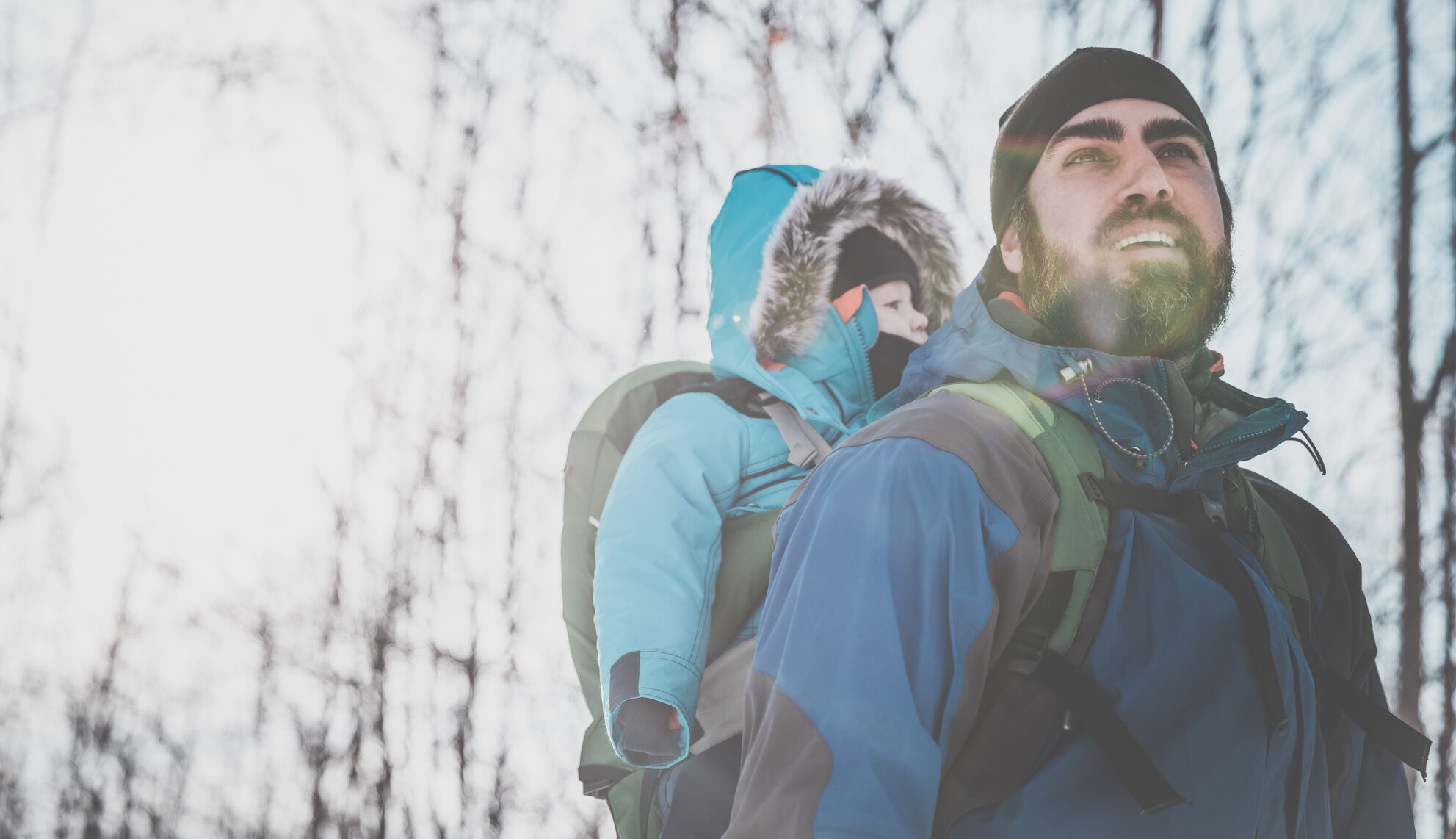 A young father hiking in a winter landscape with a baby in a carrier.