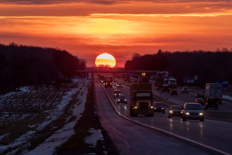 A large red sun behind an overpass with traffic in the foreground.