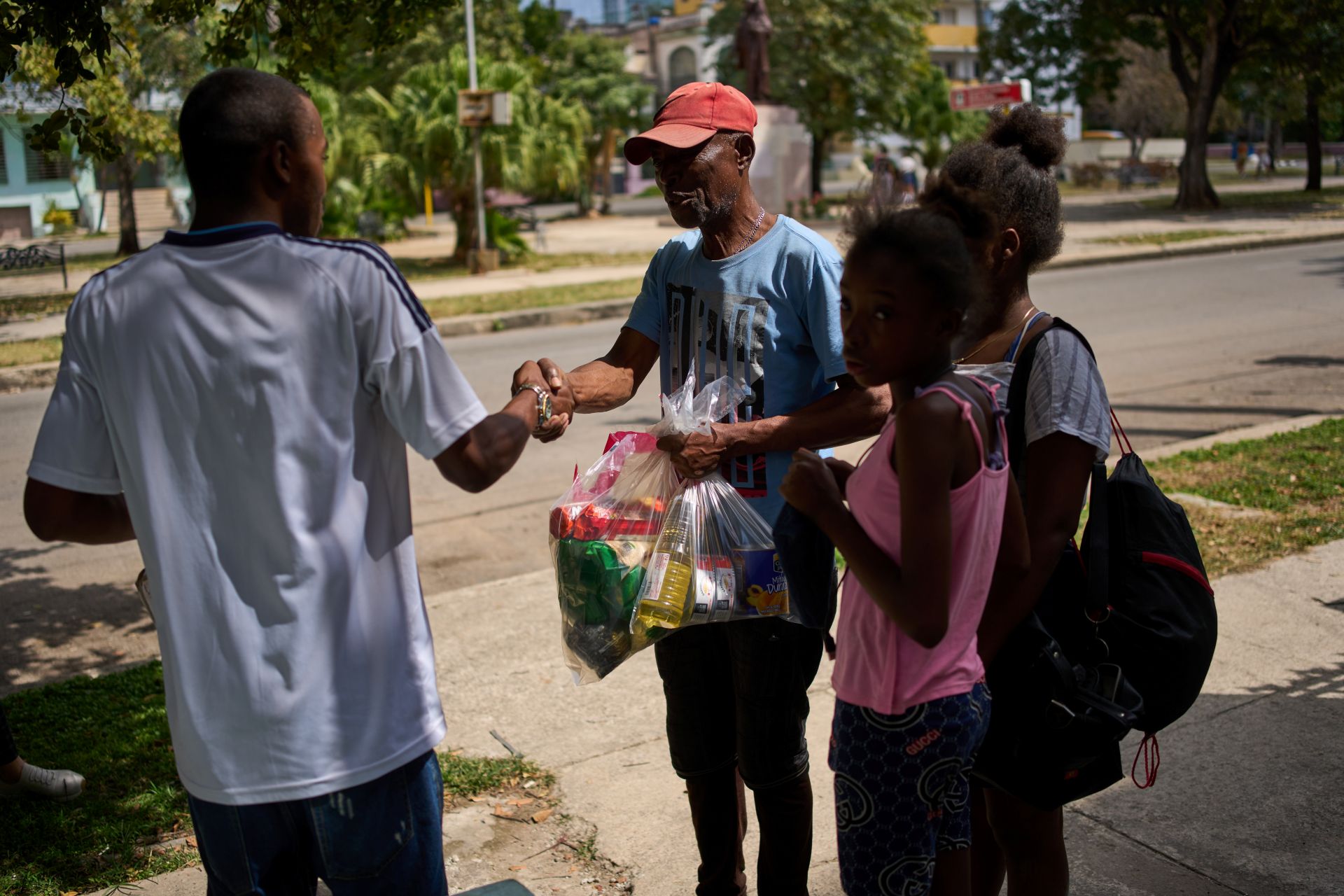 A family of three including a young girl receives clear plastic bags of groceries including cooking oil from a man.