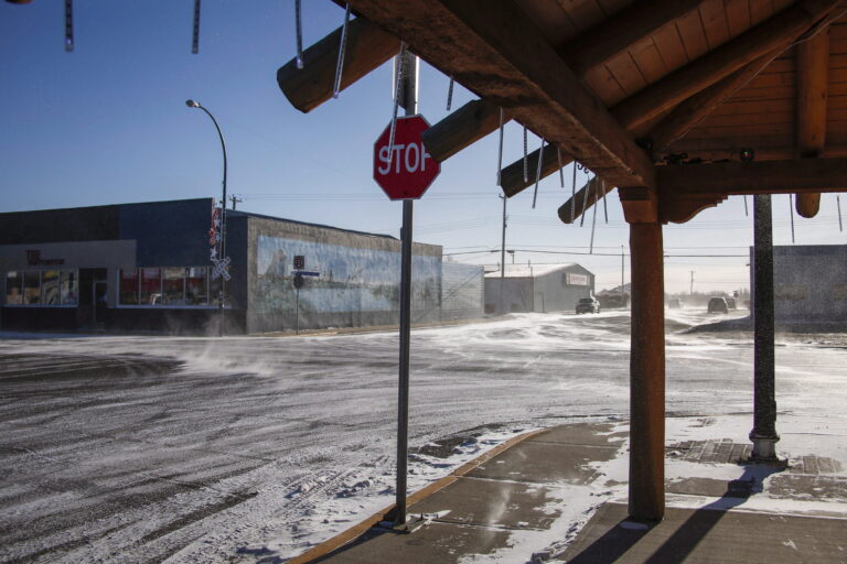 Le vent chasse la neige à travers une intersection principale sans aucune personne visible.
