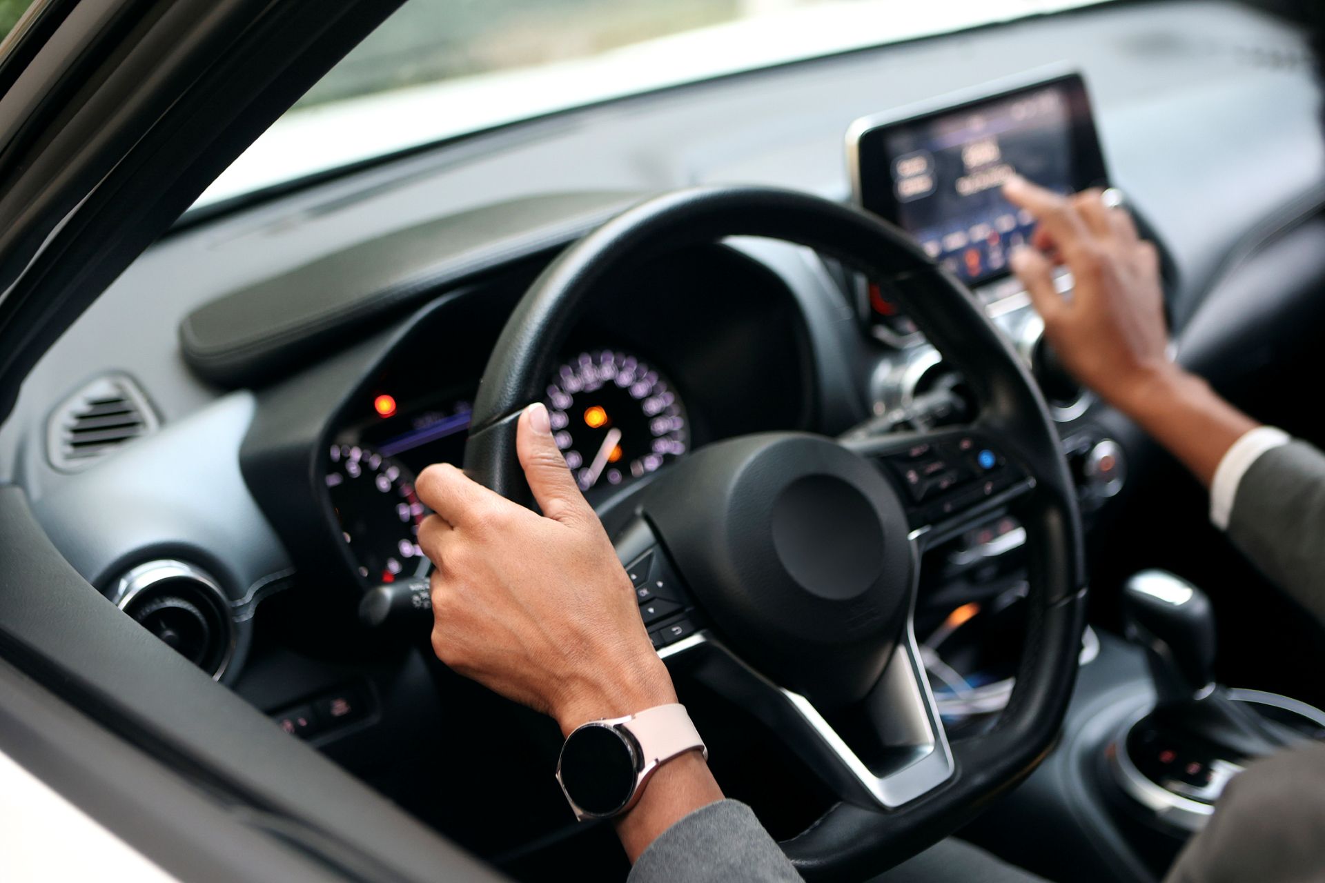 A driver at the wheel of a car, putting a finger to the touchscreen in the dashboard.