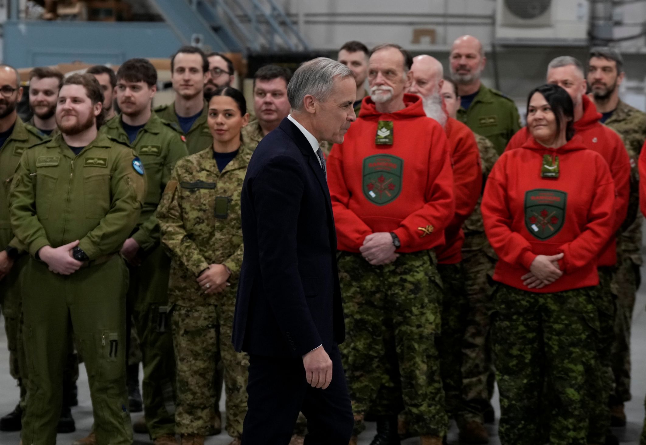 Mark Carney walking past a line of soldiers, including Canadian Rangers wearing their bright red hooded sweaters.