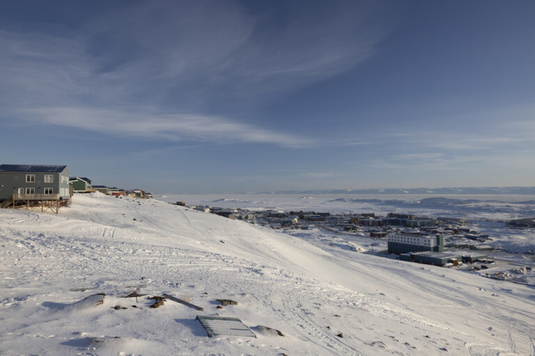 A wide angle on Iqaluit from ridge above it in winter, under a mostly blue sky.
