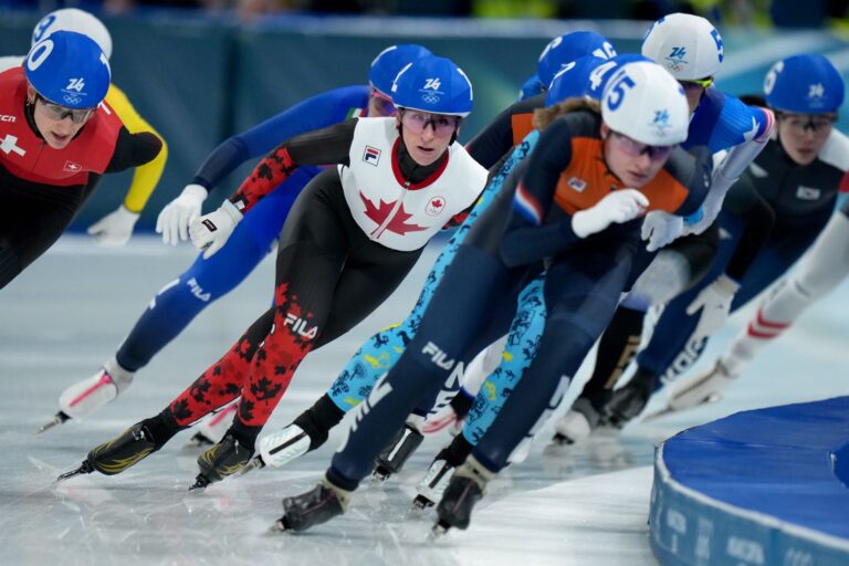 A pack of eight skaters lean hard into a curve.