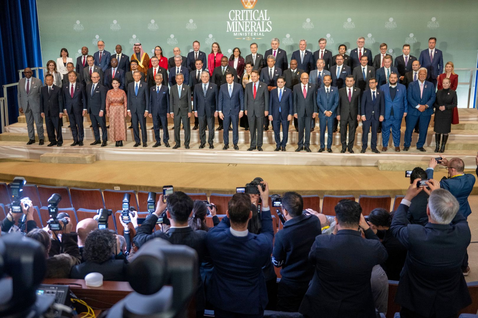 Dozens of ministers stand in a family photo while a dozen photographers jockey for the shot in the foreground.