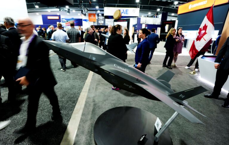 People browse company booths, one of which includes a model of a fighter jet.