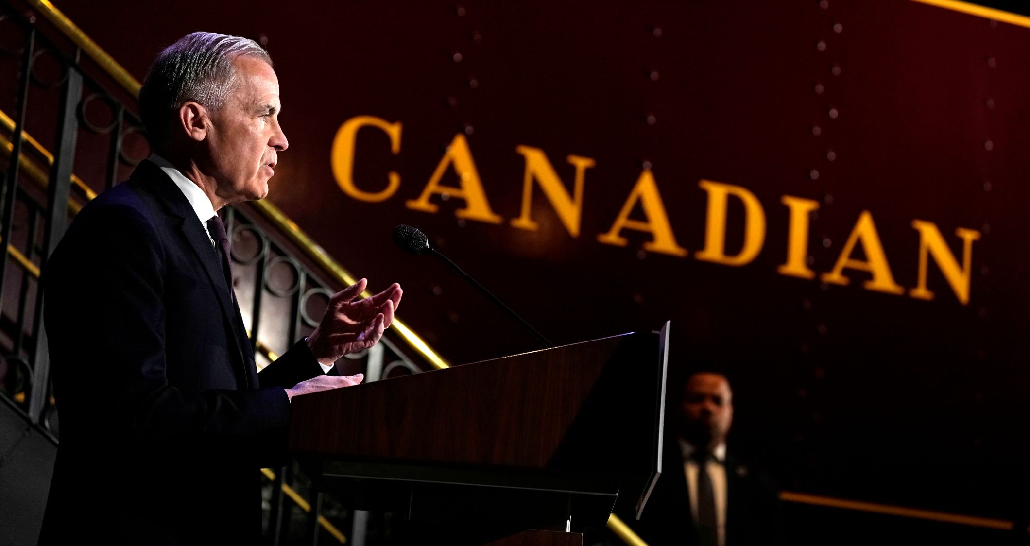 Mark Carney photographed in profile with an old Canadian Pacific train in the background. The word “Canadian” appears in front of him.