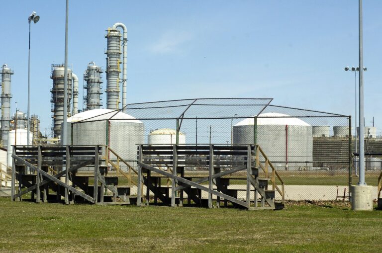 A baseball diamond in the foreground with a chemical plant in the background.