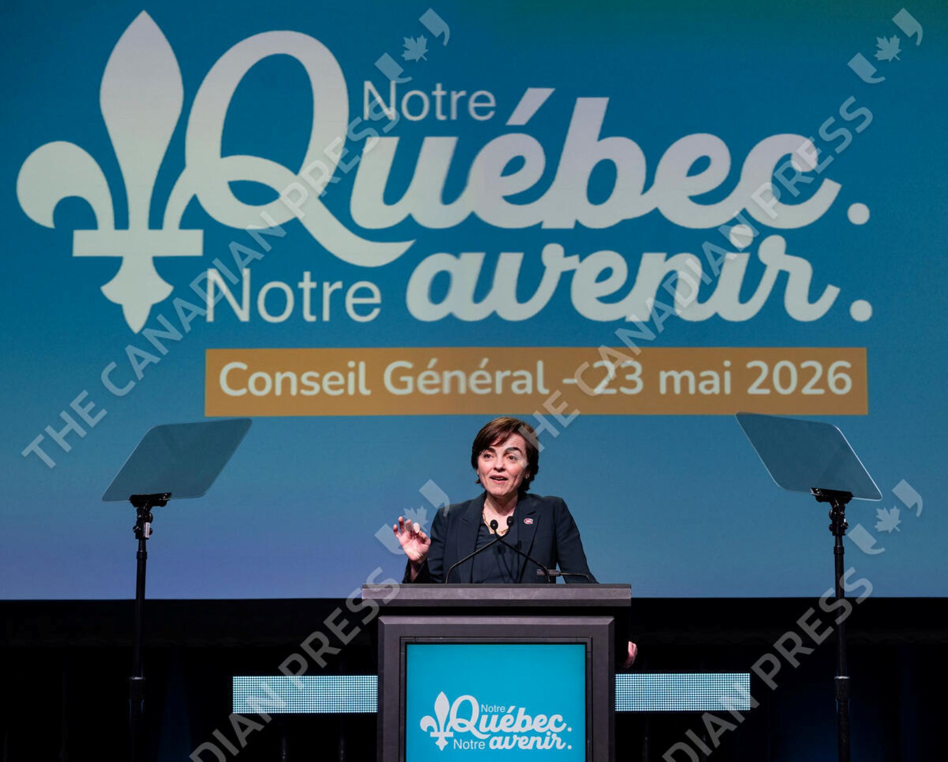 La ministre Christine Fréchette prononce un discours derrière un lutrin lors du Conseil général de la Coalition Avenir Québec, le 23 mai 2026. En arrière-plan, un grand écran bleu affiche le slogan « Notre Québec. Notre avenir. » accompagné du logo fleurdelisé du parti.