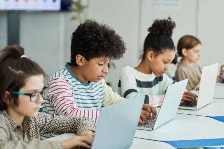 Four young children using laptops sitting at a table side by