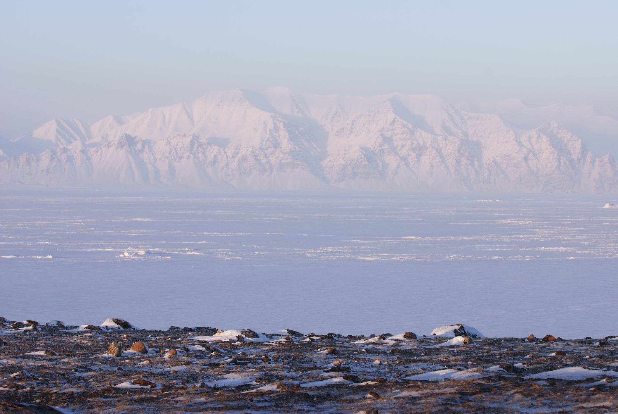 An ice-packed inlet with snow-covered mountains in the background.