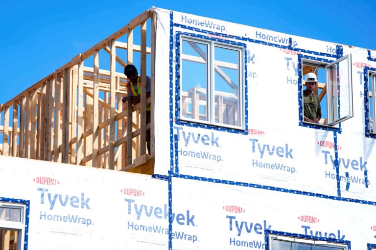 Deux ouvriers se penchent par les ouvertures de la fenêtre et de la charpente en bois de l'étage supérieur d'une maison en construction.