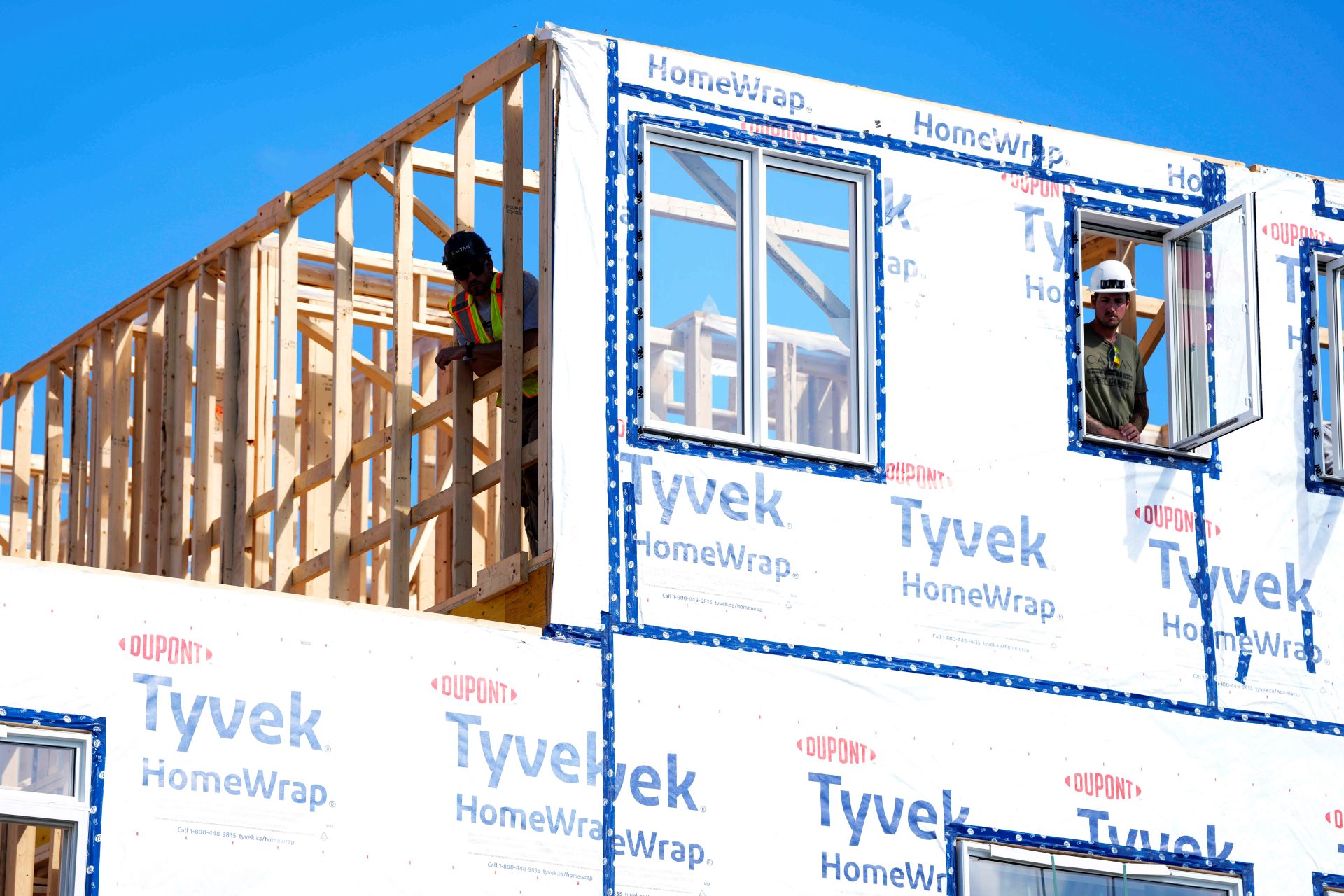 Deux ouvriers se penchent par les ouvertures de la fenêtre et de la charpente en bois de l'étage supérieur d'une maison en construction.