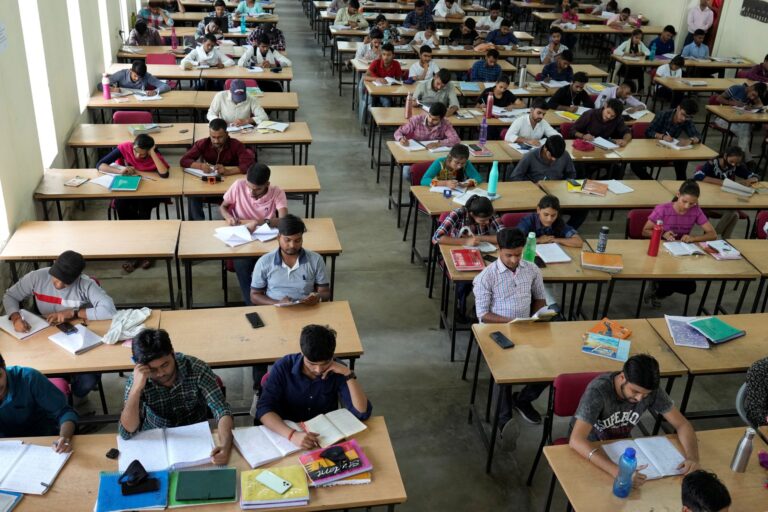 Row after row of university students sitting at tables in a large hall.