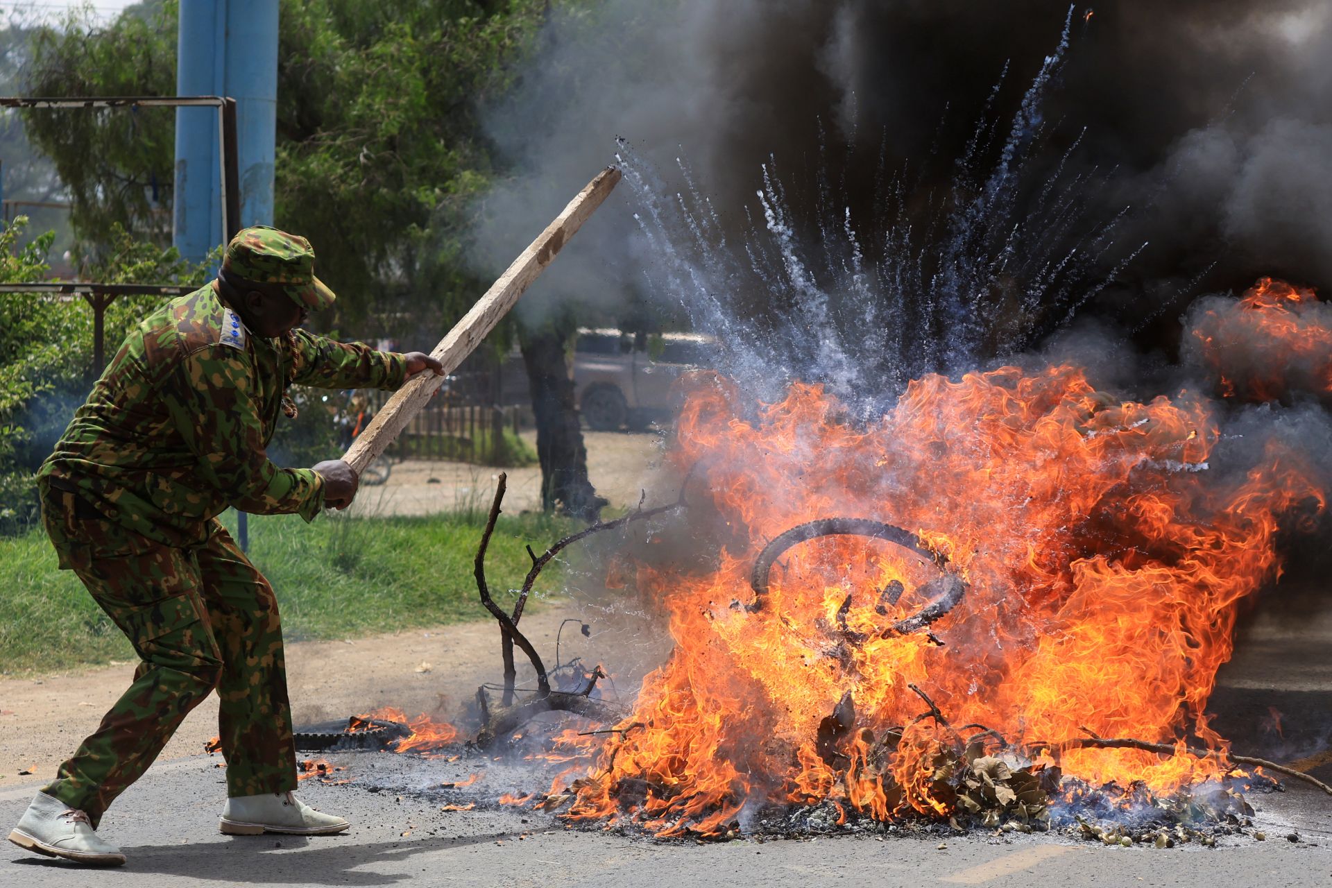 A police officer in camouflage strikes at a fire with a stick.