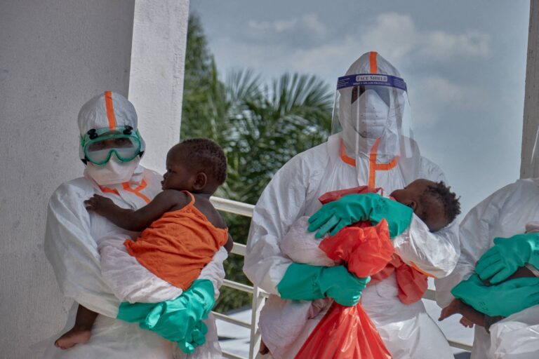 Healthcare workers wearing Ebola protective suits hold two young children at a treatment center in Bunia, Democratic Republic of Congo.