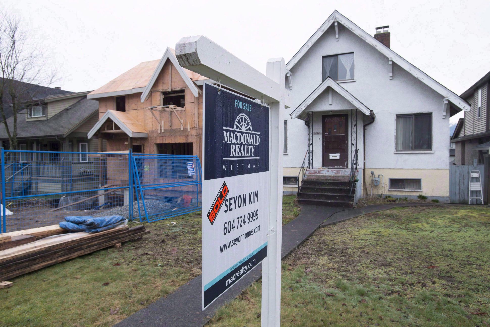 Panneau « À vendre » devant une maison unifamiliale à Vancouver, à côté d’un chantier de construction résidentielle dans un quartier urbain.