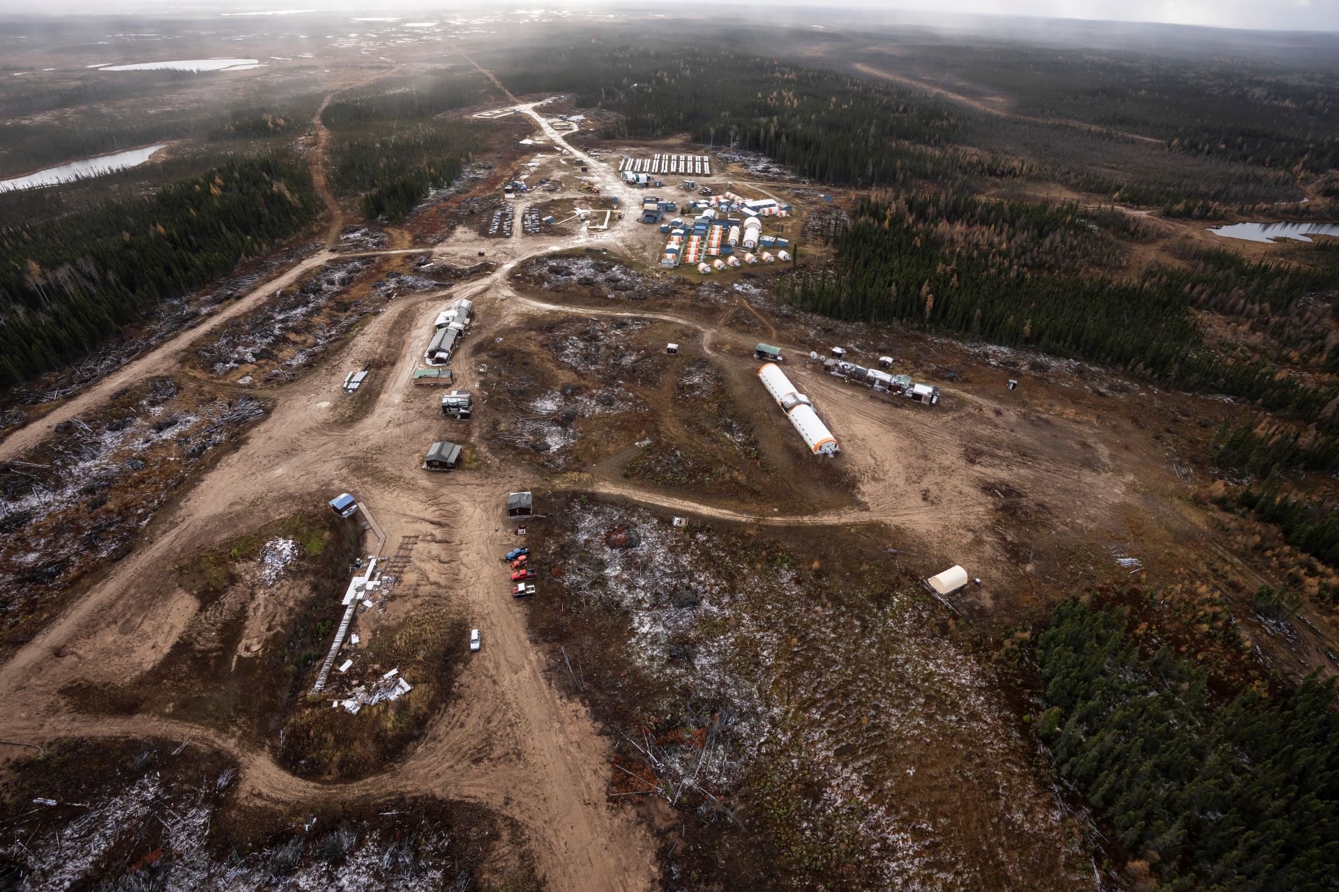 Aerial view of dirt roads cut into a forested area, with low-rise structures clustered throughout. 