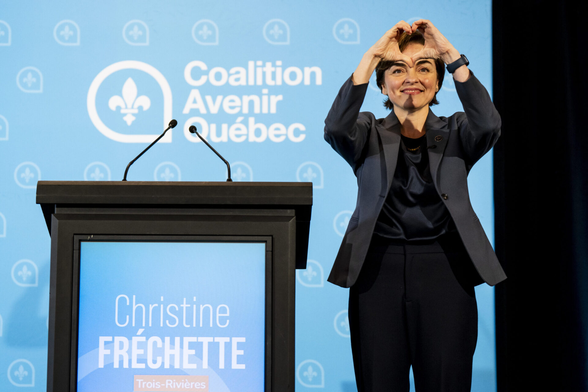 Christine Fréchette est debout et forme un coeur avec ses mains durant une conférence de presse.