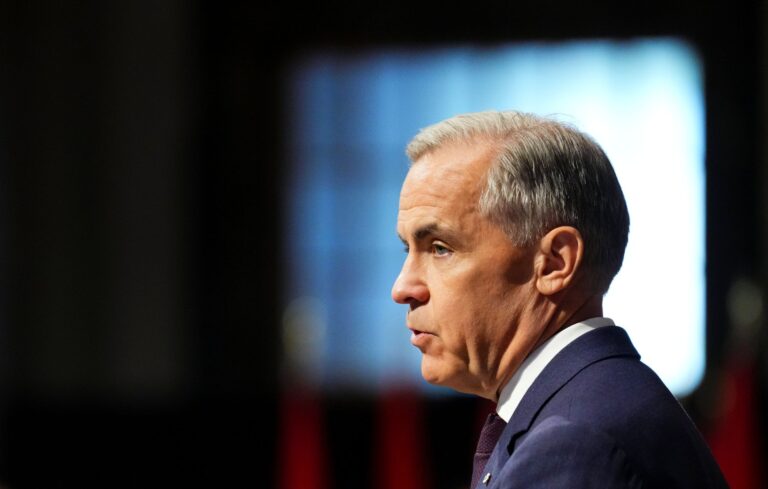 Mark Carney de profil devant un écran sur fond noir.