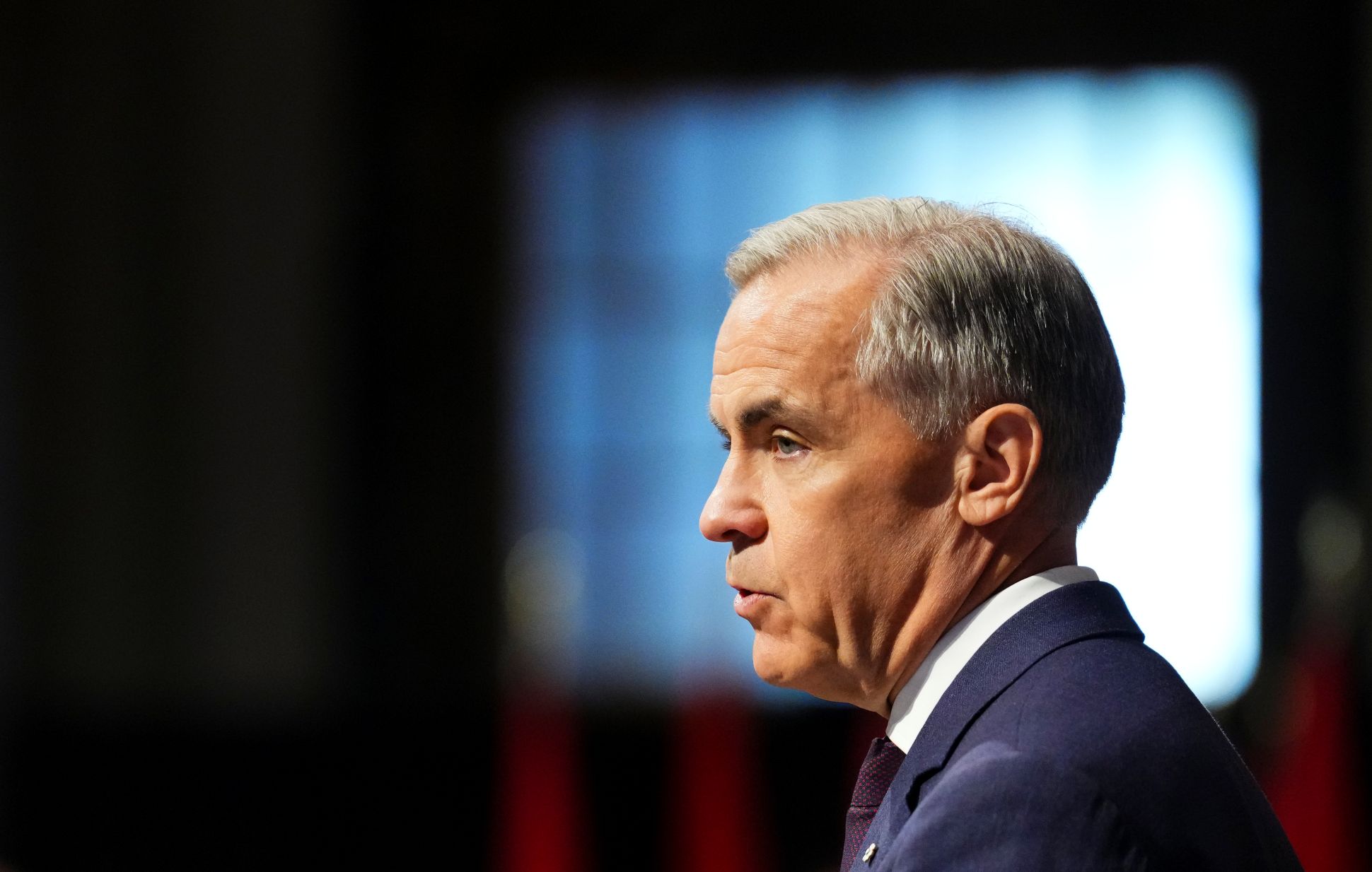 Mark Carney de profil devant un écran sur fond noir.