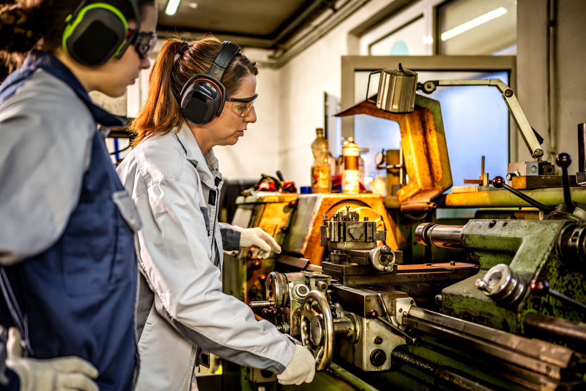 Caucasian woman operates a metal lathe in an industrial setting.