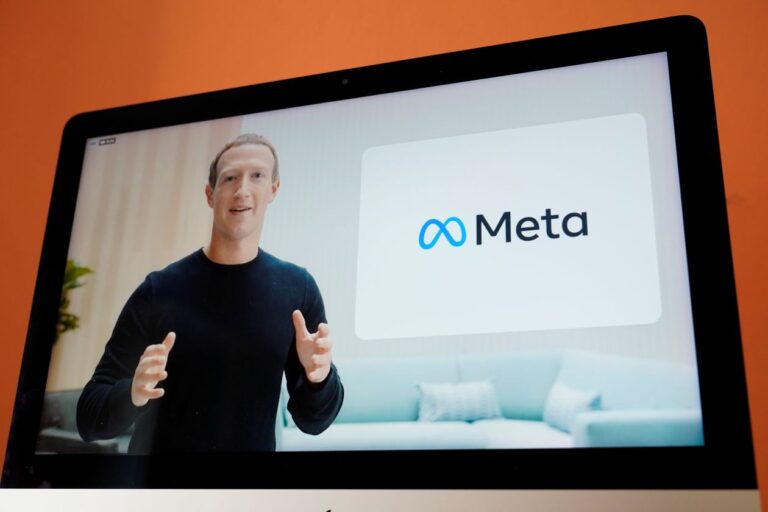 Mark Zuckerberg seen on a laptop screen giving a presentation with the Meta logo to his left.