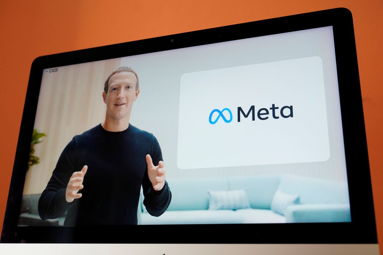 Mark Zuckerberg seen on a laptop screen giving a presentation with the Meta logo to his left.
