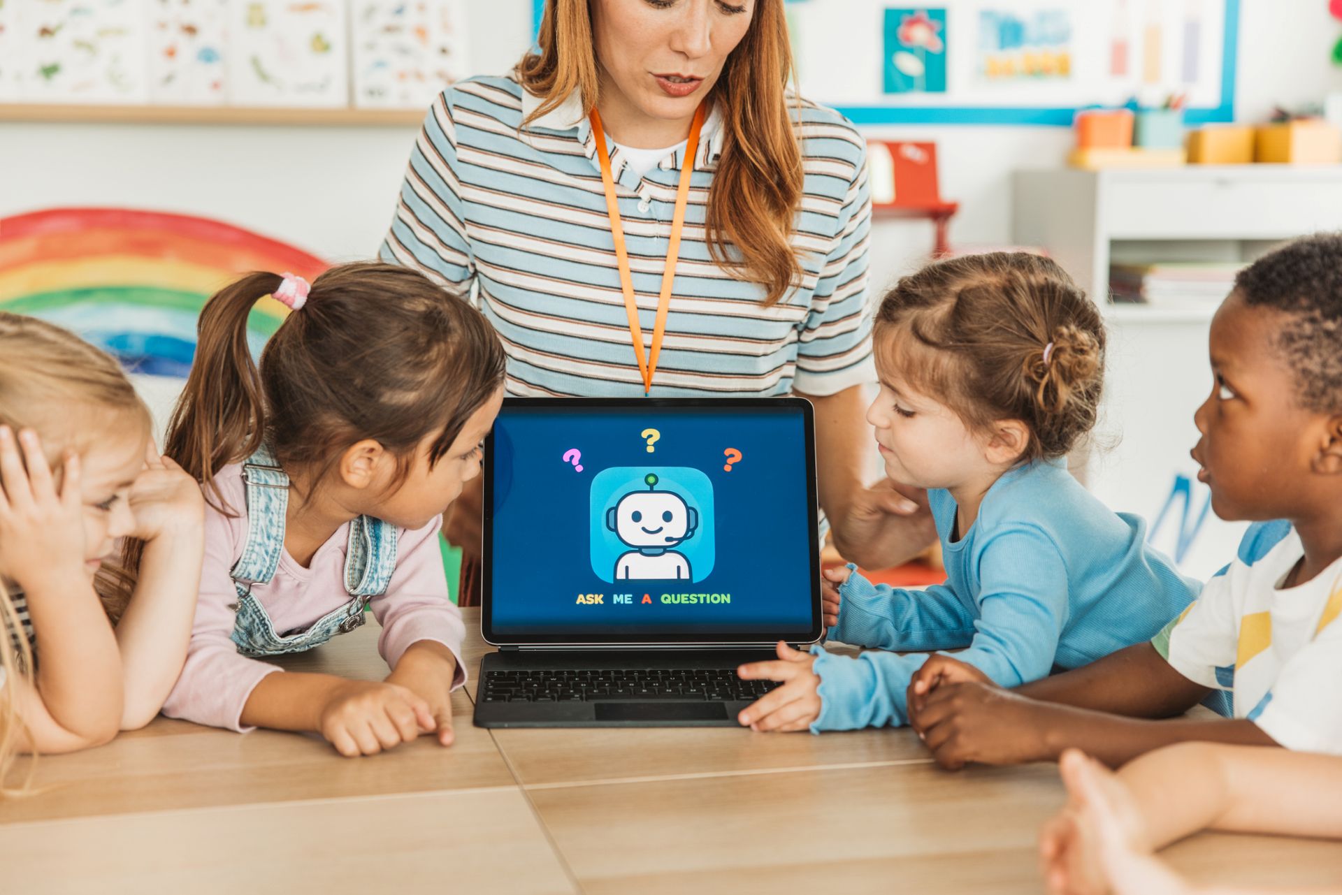 Four children gathered around a laptop with an adult standing behind it.