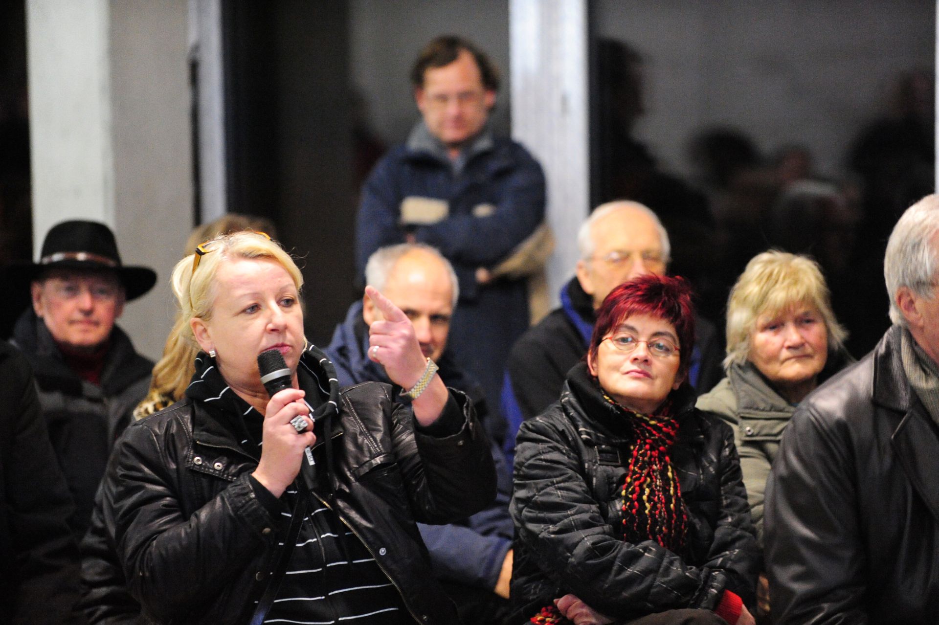 A woman holding a microphone gestures with her hand as other citizens look on.