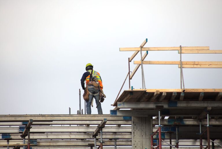 Construction workers Alt text: Single worker stands on a partially framed house.