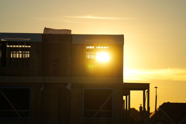 A sun sets behind the frame of a new home construction.