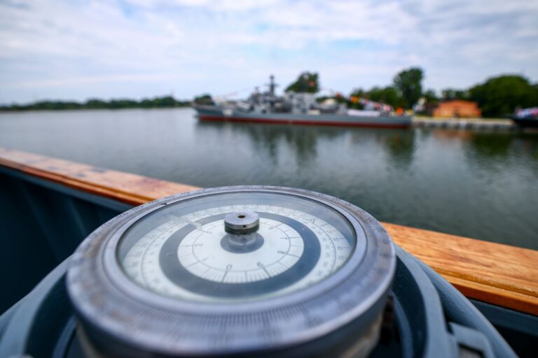 A closeup of a nautical compass with water and land in the background.
