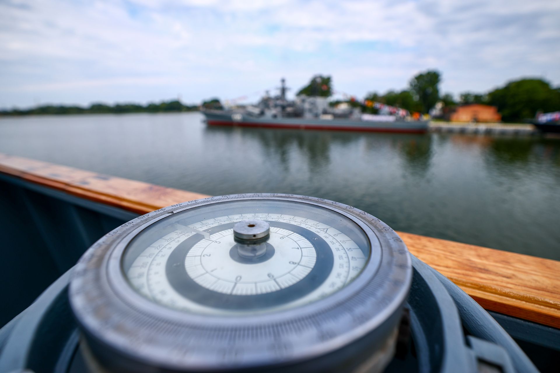 A closeup of a nautical compass with water and land in the background.