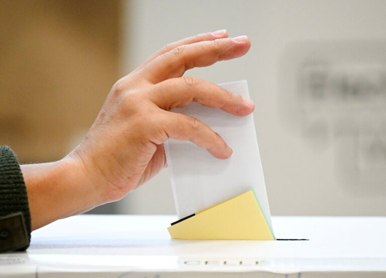 Une main dépose un bulletin de vote dans une boîte de scrutin.