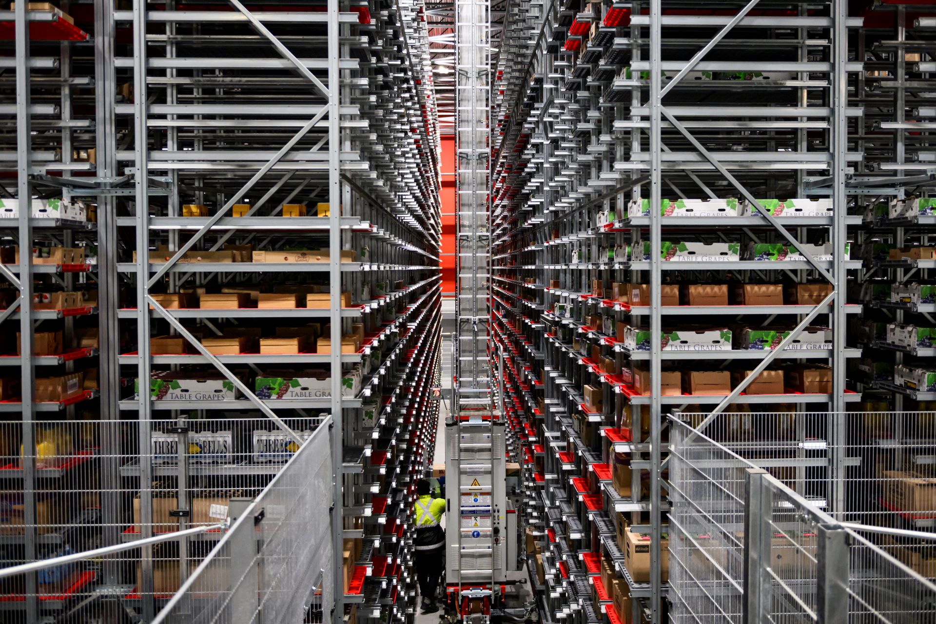 The warehouse space is filled with many metal shelves that reach several storeys high. Fruit and vegetables sit in boxes as far as the eye can see.