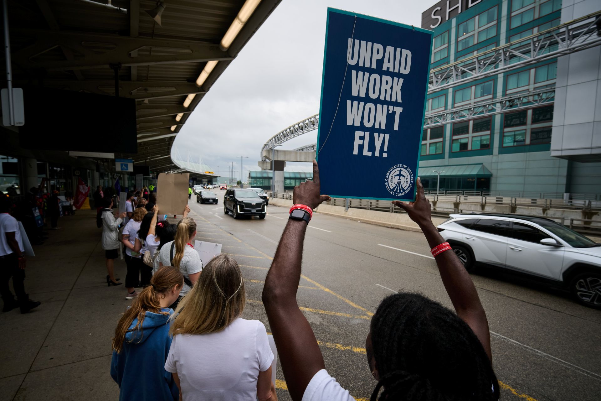 As he stands in a line of his coworkers, a man holds a sign high in the air that says: “Unpaid work won’t fly.”