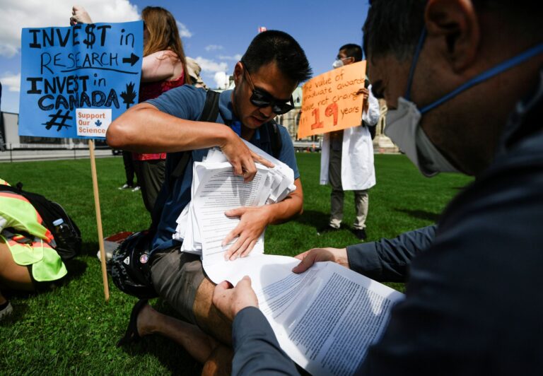 A man wrangles a long bundle of printed paper in front of Parliament.